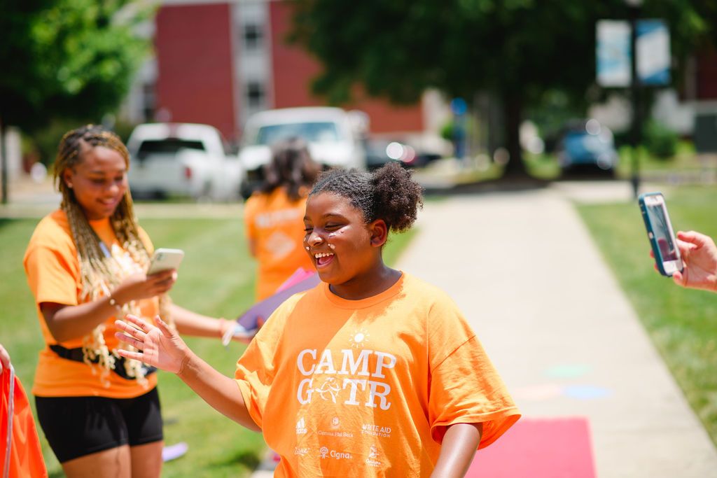 a Camp GOTR participant smiles in a yellow shirt while high-fiving her teammates